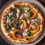 Artisan pizza with sliced apricots, beetroot, feta cheese, and arugula on a textured crust.